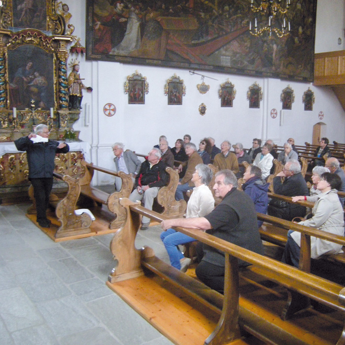 Eine Gruppe sitzt in einer Kirche und hört einem Referenten zu.